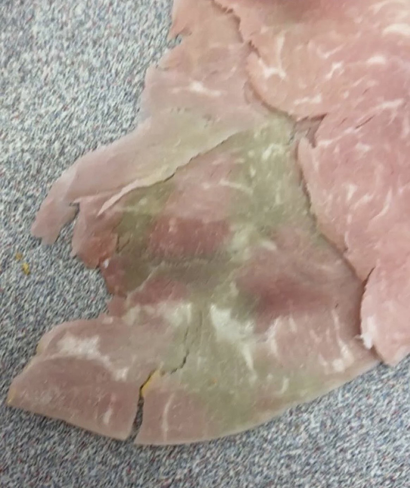 A piece of thin-sliced lunch meat placed on a granite-patterned surface shows discoloration of green and gray patches.