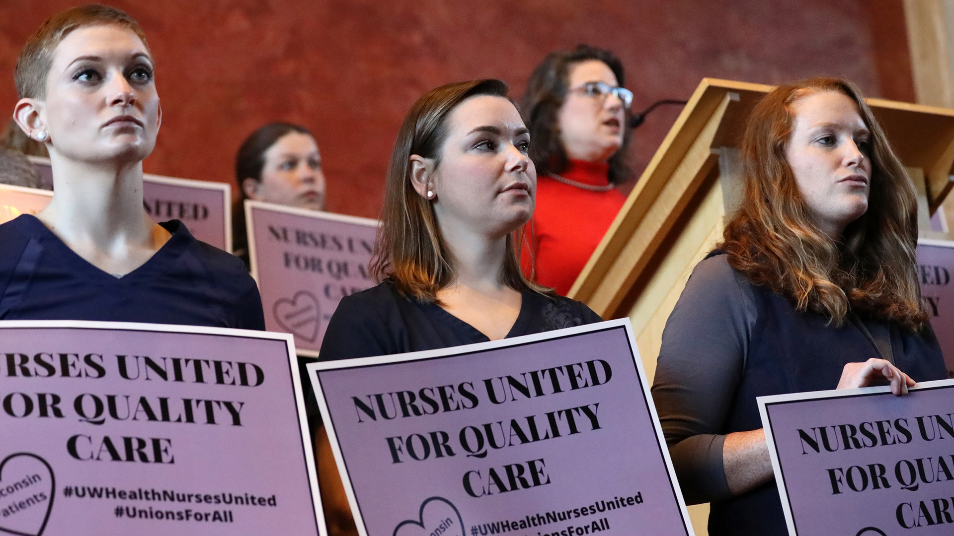 Courtney Maurer and others stand in a line while holding a sign that reads "Nurses United for Quality Care," with more people holding these signs in the background.