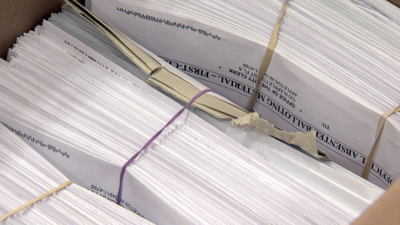 Bundles of absentee ballot envelopes sit inside a cardboard box.