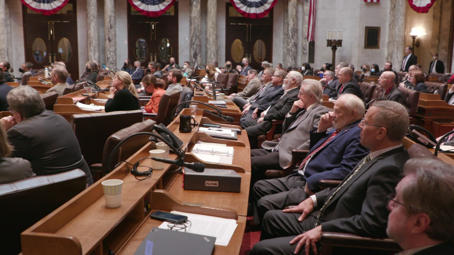 Members of the Wisconsin Assembly sit at their desks and listen to a speech.