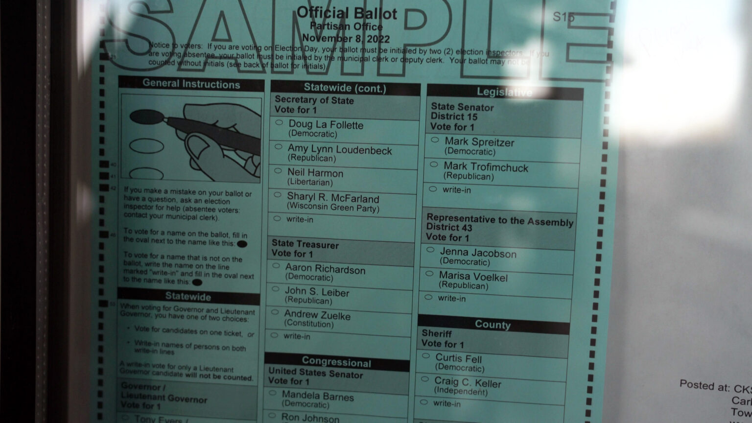An official ballot for the November 8, 2022 election with a large stenciled-stamp reading SAMPLE across its top is visible in a glass display case.