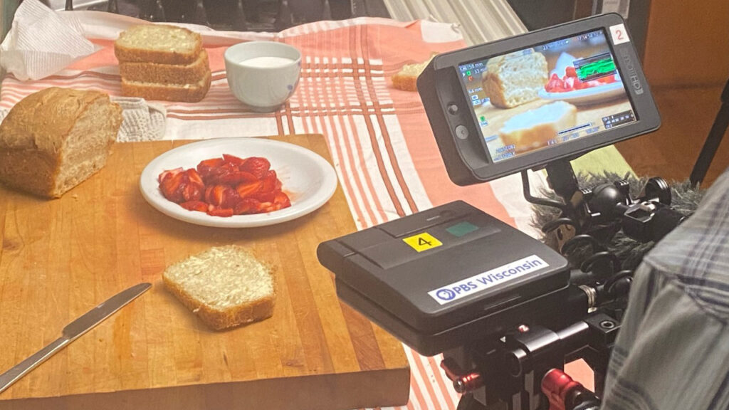 A cameraman captures footage of strawberry jam styled on a board with bread and butter.