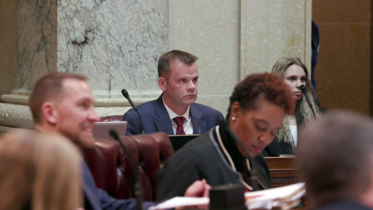Devin LeMahieu sits at his desk in the chambers of the Wisconsin Senate, with other senators and staff in the foreground and background.