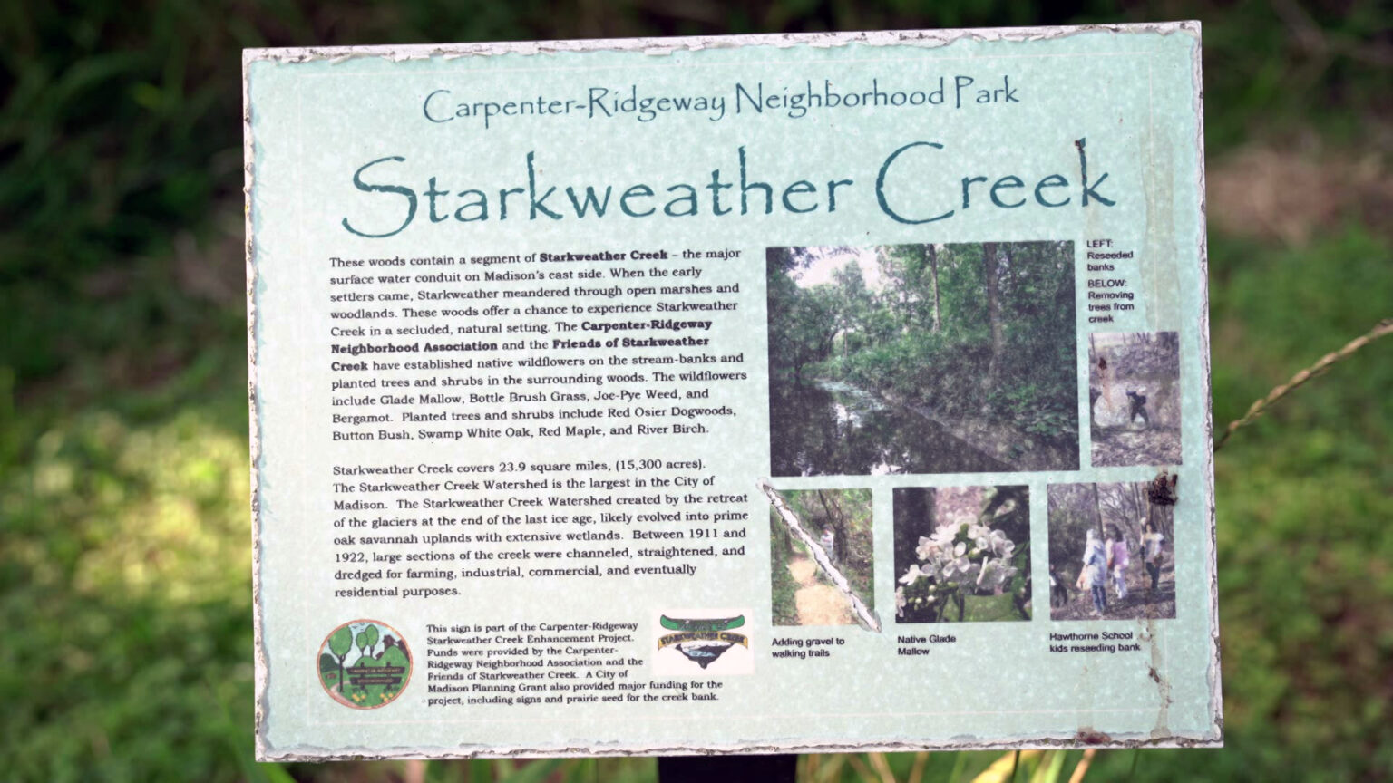 An interpretive sign with the titles Carpenter-Ridgeway Neighborhood Park and Starkweather Creek displays photos and explanatory text about the two geographic features, with foliage in the background.