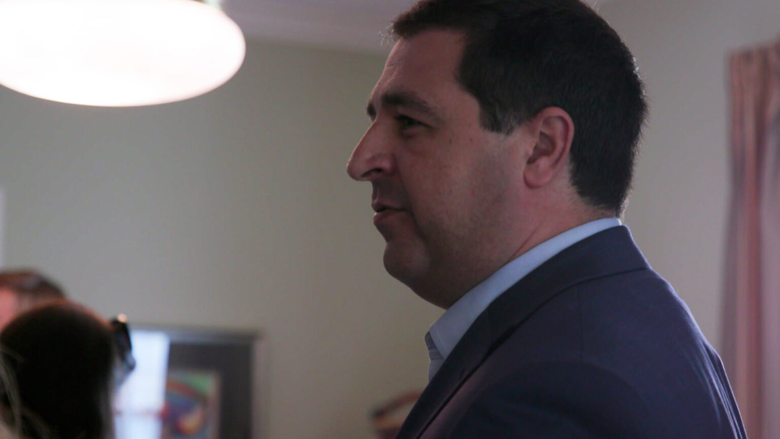 Josh Kaul stands in a room while talking with other people.