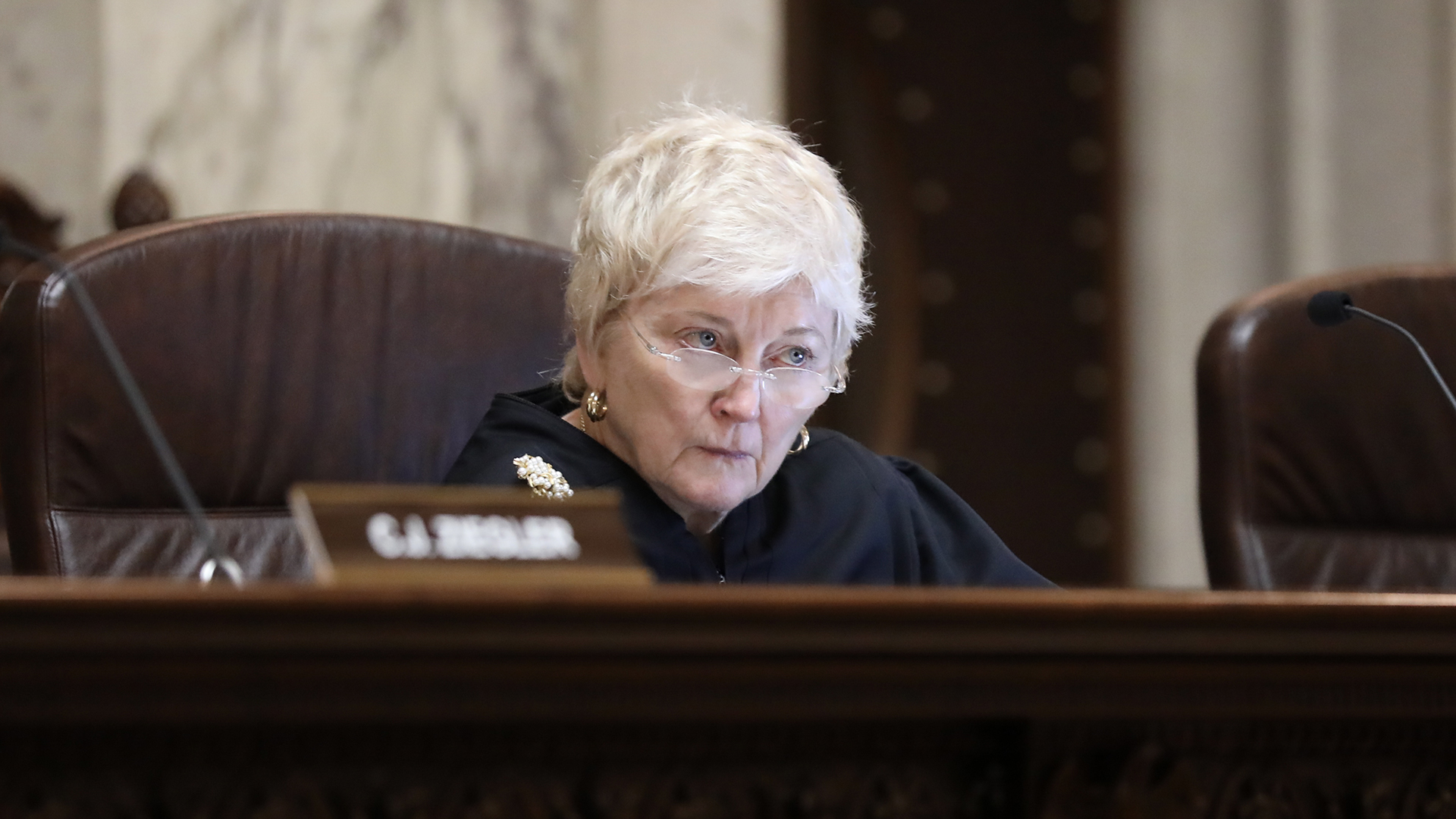 Patience Roggensack sits in a chair behind a judicial bench and listens to another speaker.