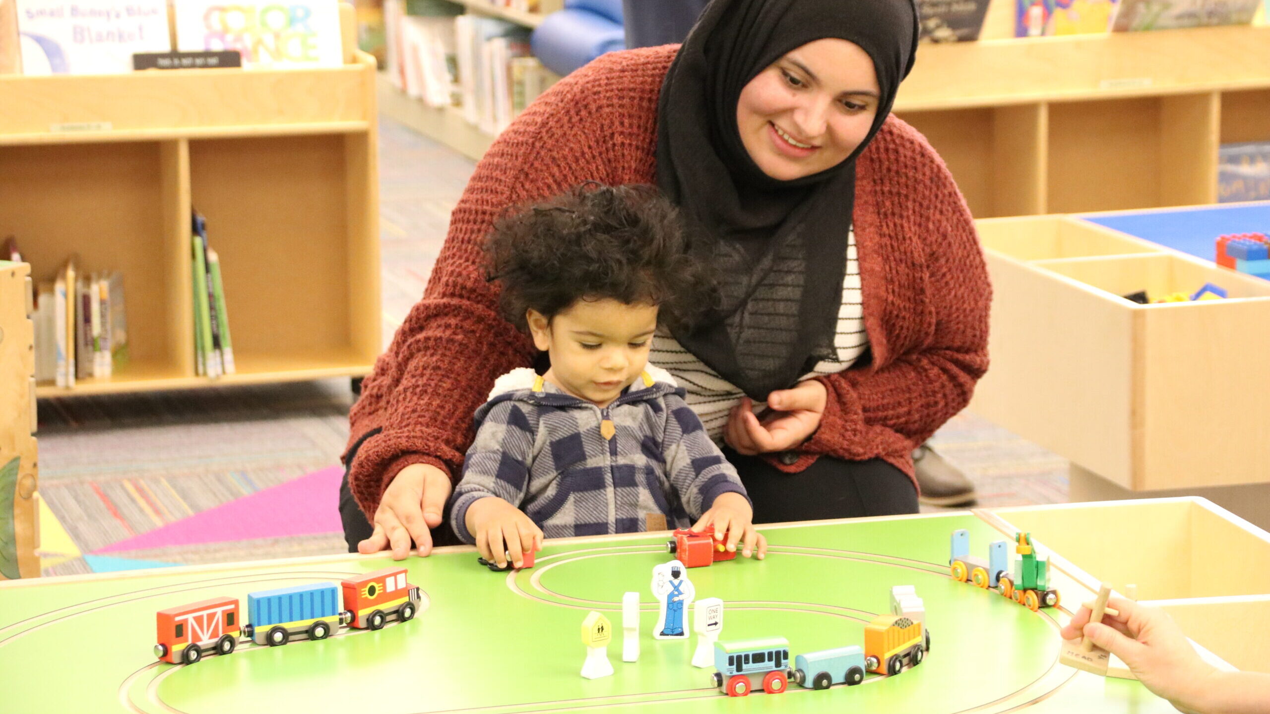 A woman and child play at a train table in a library