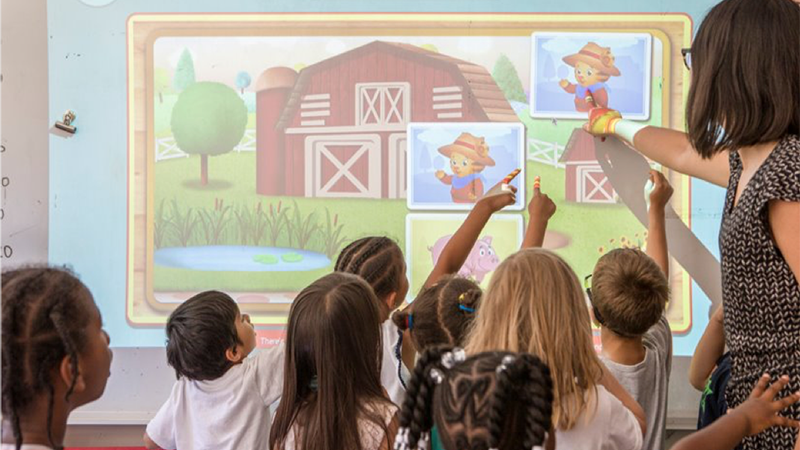 A teacher and students point to images from Daniel Tiger's Neighborhood on a smart board.