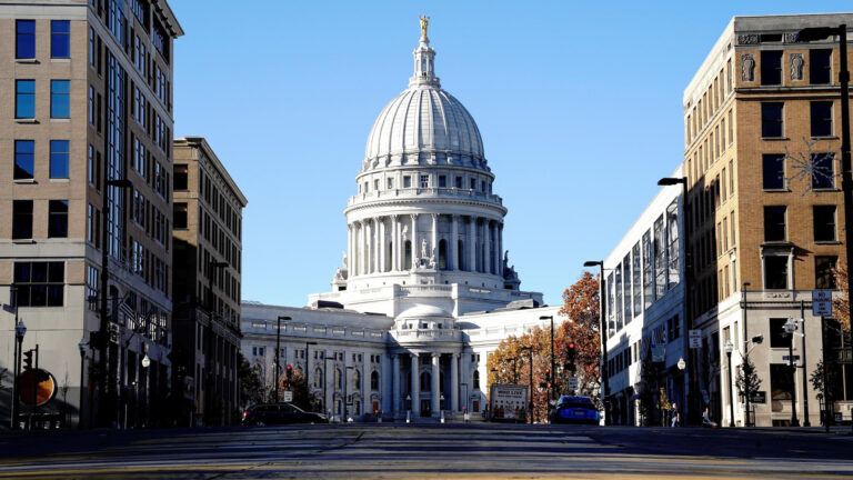 The Wisconsin State Capitol stands behind two rows of buildings on either side of one block of a road.