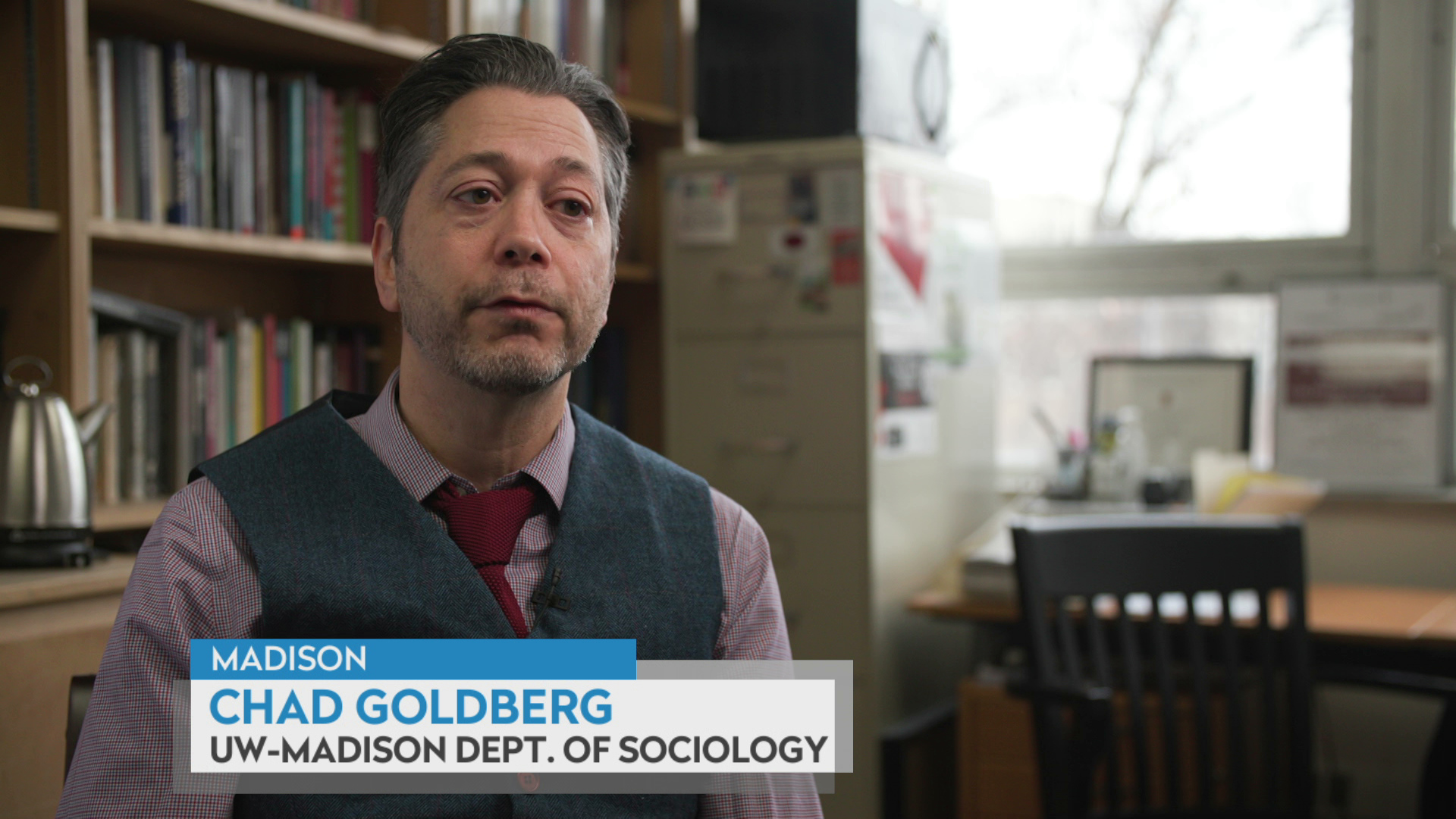 Chad Goldberg sits in an office with bookshelves, a file cabinet, window, desk and chair in the background, with a graphic at bottom reading "Madison," "Chad Goldberg," and "UW-Madison Dept. of Sociology."