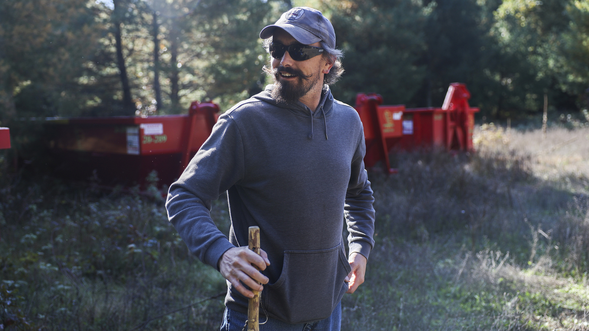 Zach Skrede stands in a field in front of multiple construction dumpsters, with trees in the background.