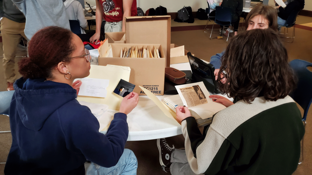 Three high school students sit at a table looking through archival photos and newspaper articles.