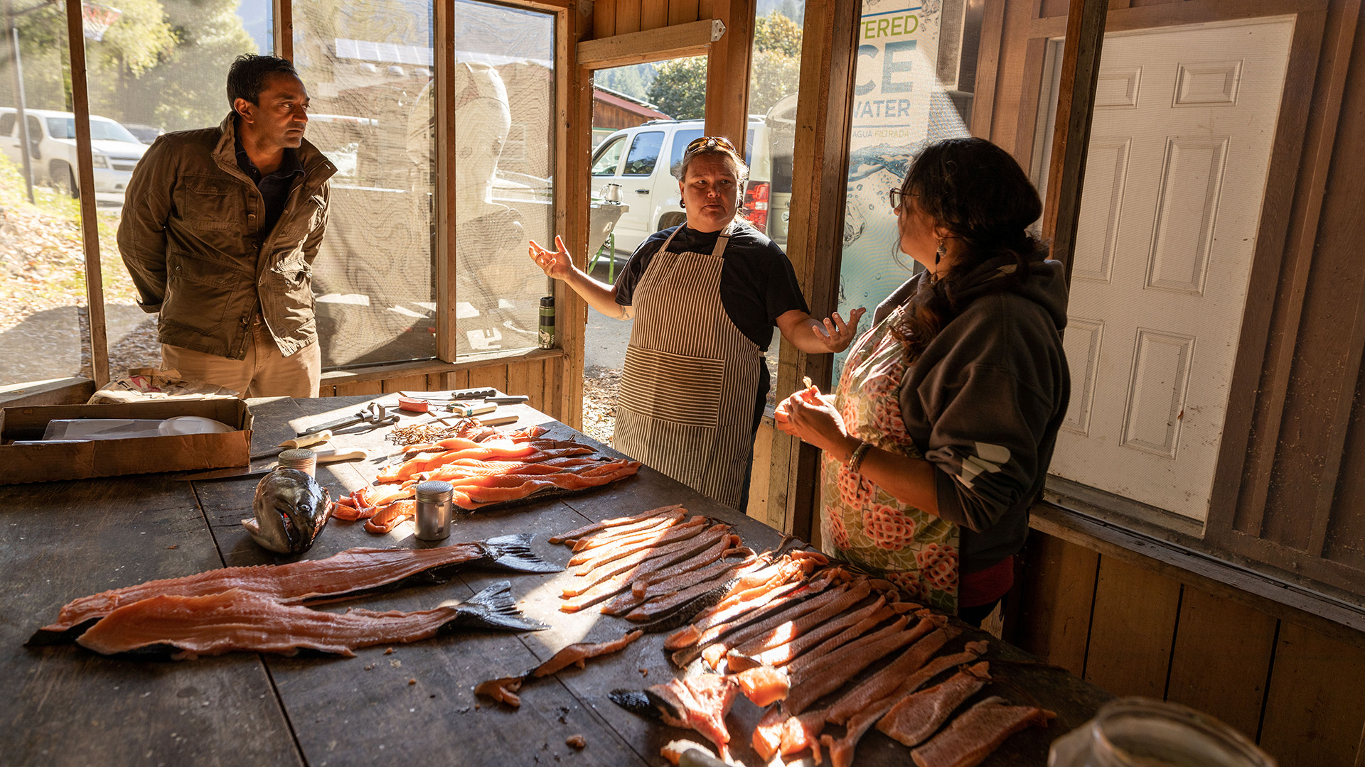 Two women and a man inside a fish smoke house.