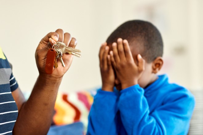 A boy with his hands over his eyes is listening as an adult shakes keys in front of him.