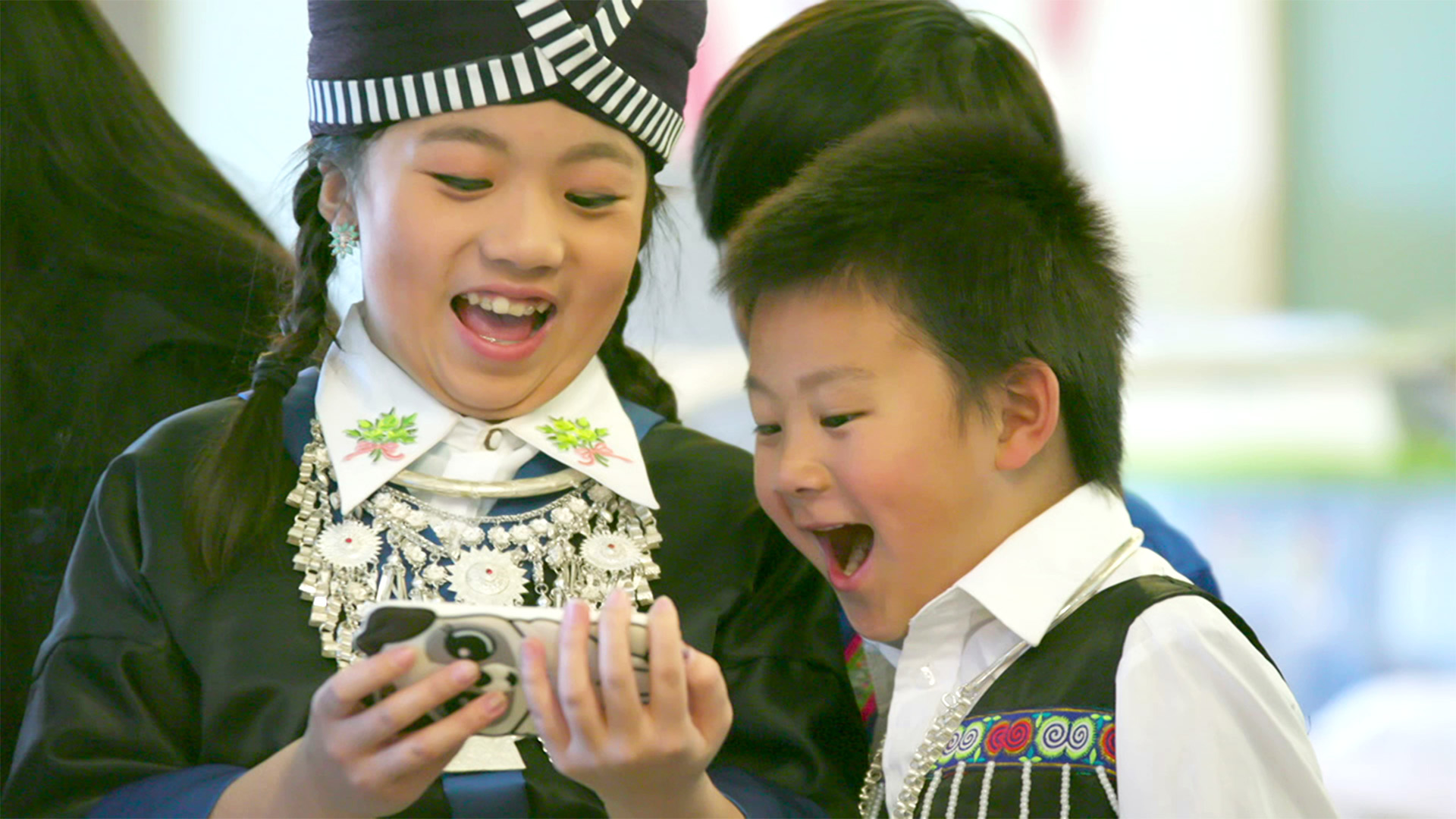 Two Hmong children in Wisconsin smile together while looking into a smart phone.