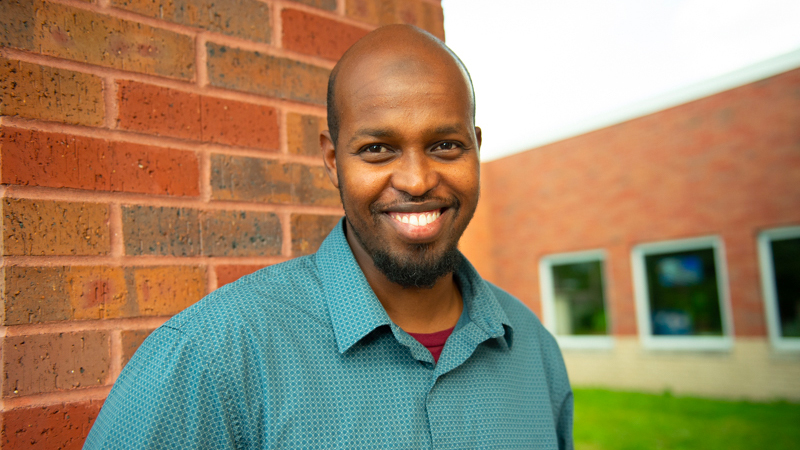 Portrait of Mohamud Farah standing in front of a red brick wall.