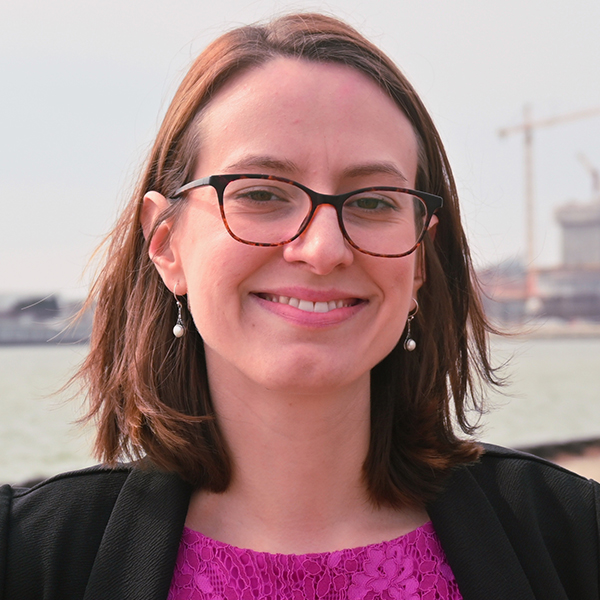 Portrait of a woman wearing glasses, smiling, and standing in front of water.