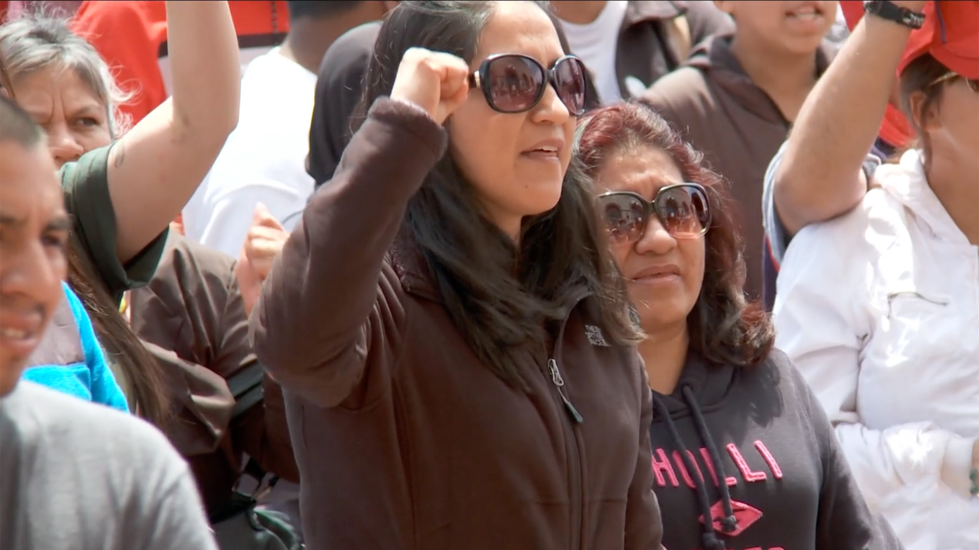 A group of Latina/o/e people in Wisconsin stand in protest. In the foreground, a young Latina woman raises her fist.
