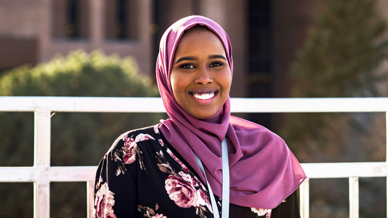 Portrait of Yasmin Nur standing in front of a white fence.