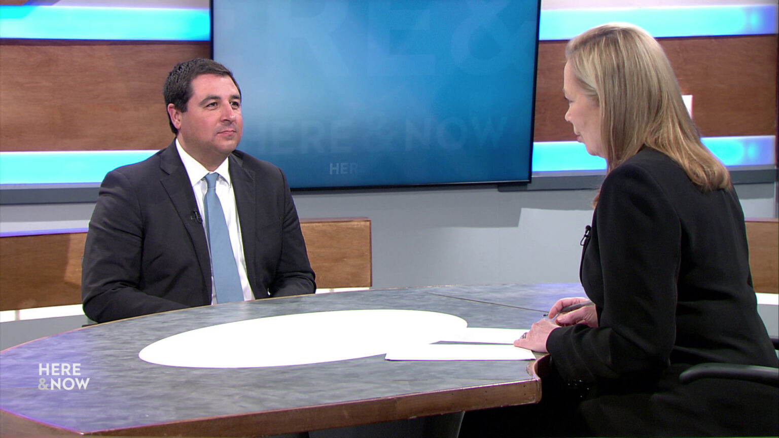 Josh Kaul and Frederica Freyberg sit facing each other on the Here & Now set.