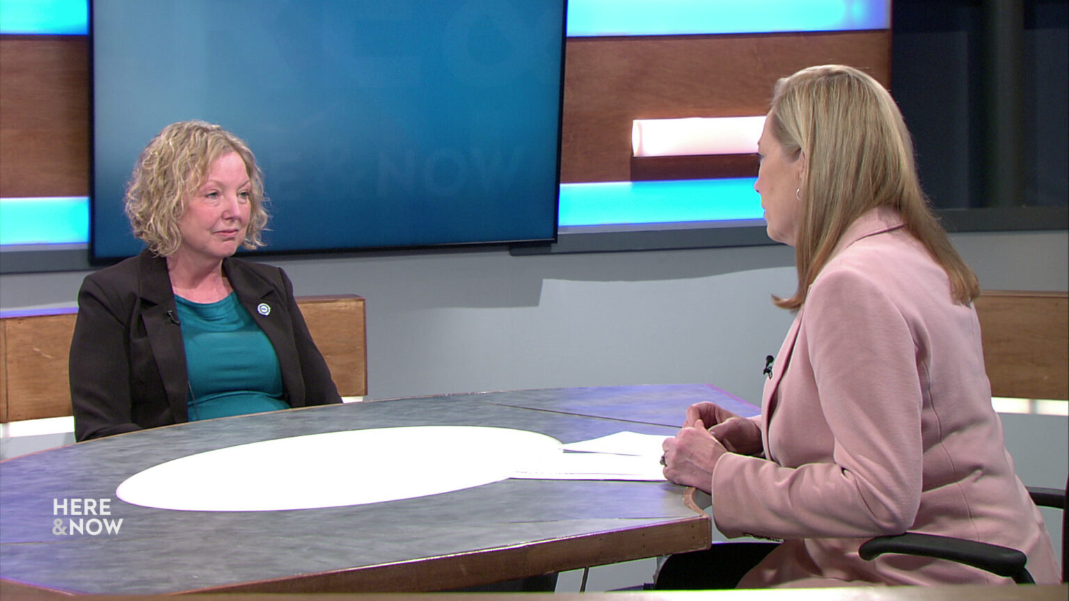 Ann Zenk and Frederica Freyberg sit facing each other on the Here & Now set.