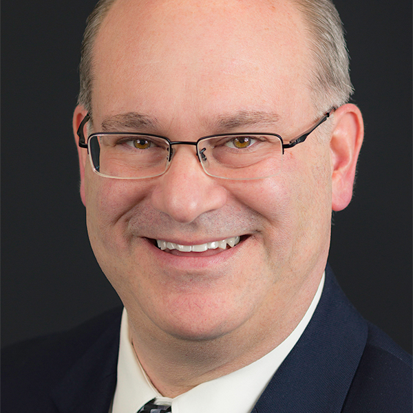 Portrait of a man (Scott Seyforth) wearing a suit, glasses and smiling.