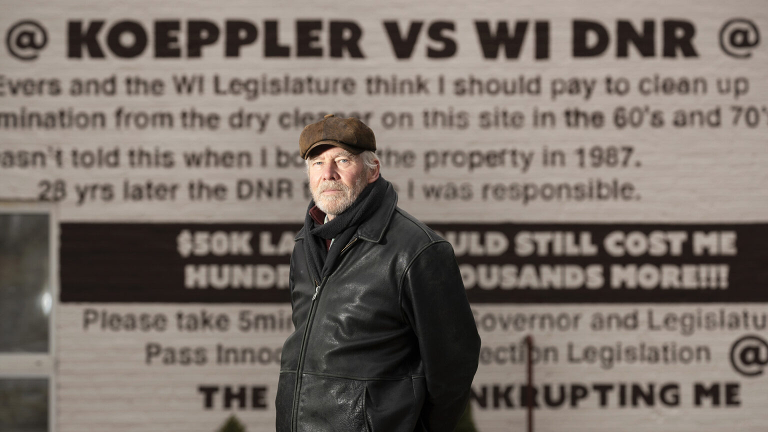 Ken Koeepler stands in front of a building painted with messages criticizing the Wisconsin Department of Natural Resources for its actions with regards to the property.