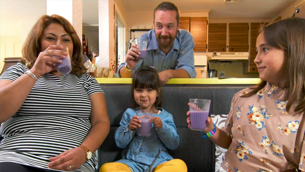A family sits on a couch with glasses of blueberry milk.