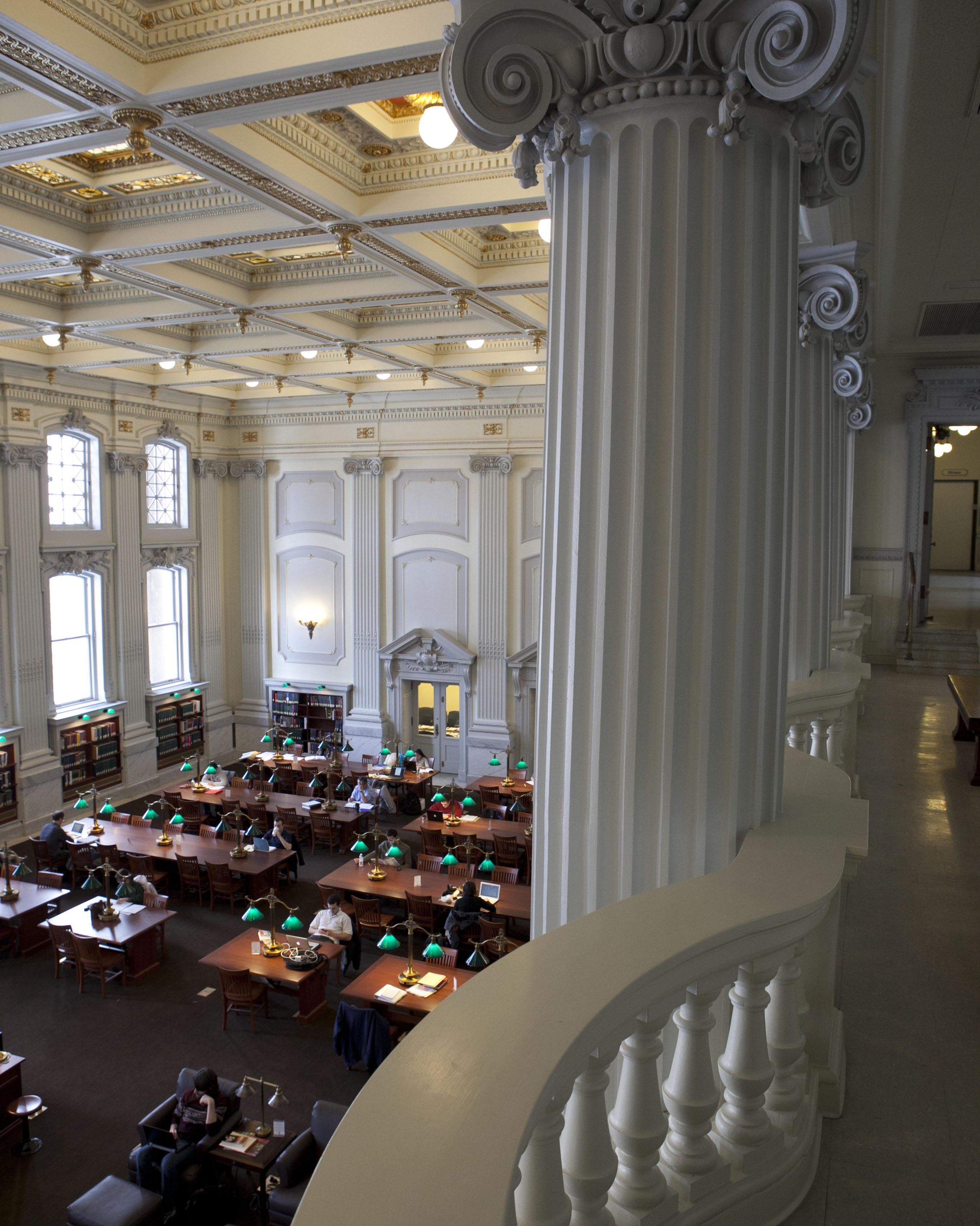 A balcony view of the Wisconsin Historical Society Reading room showing long wooden tables, chairs, and reading lamps beneath an ornate ceiling.