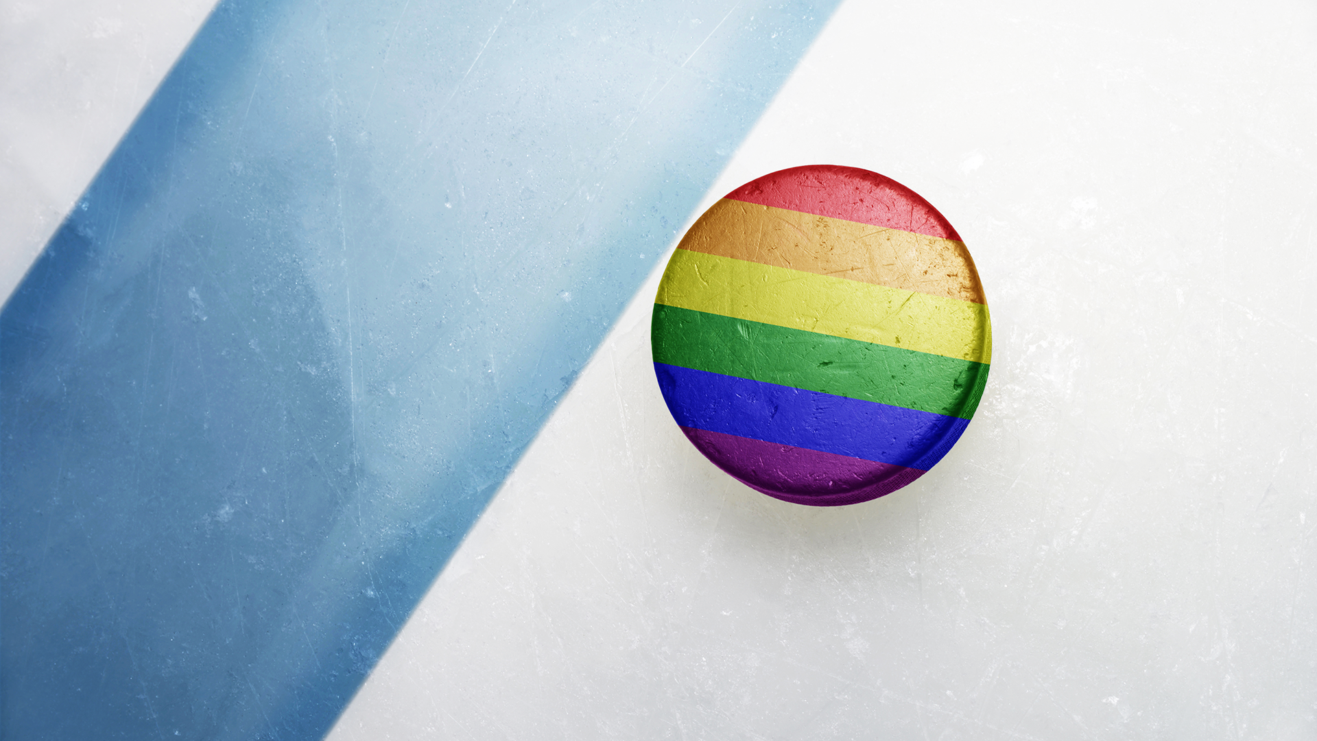A hockey puck in the colors of the rainbow Pride flag sits on ice.