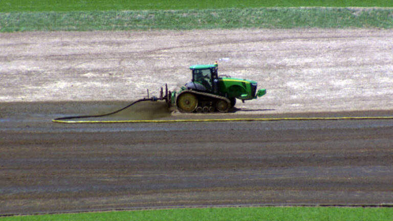 An agricultural vehicle connected to a long hose spreads liquid manure on a dry farm field.