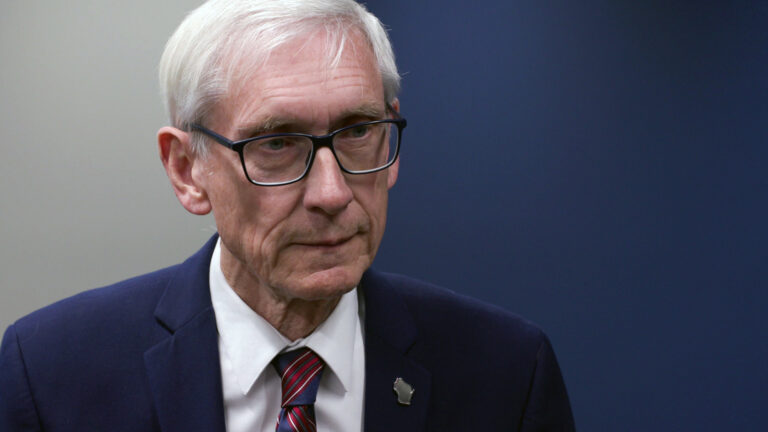 Tony Evers stands in a room and responds to questions from a reporter.