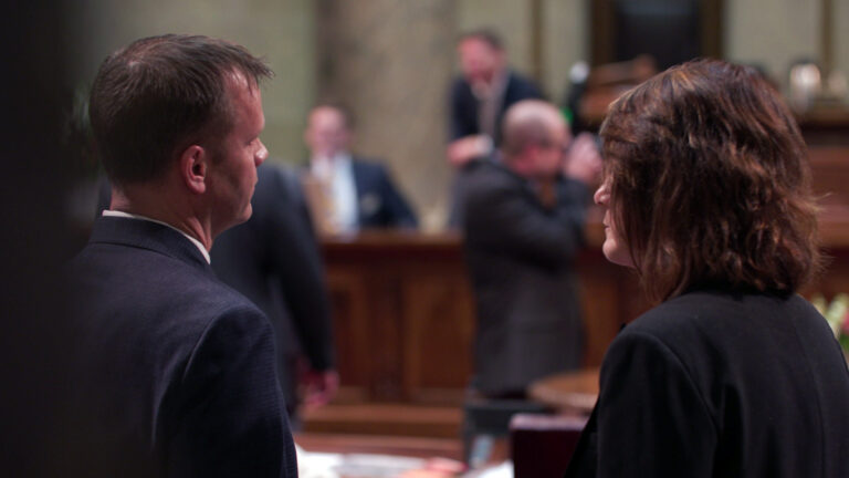 Devin LeMahieu and Mary Felzkowski speak in the Wisconsin Senate chambers, with other people standing in the background while out of focus.