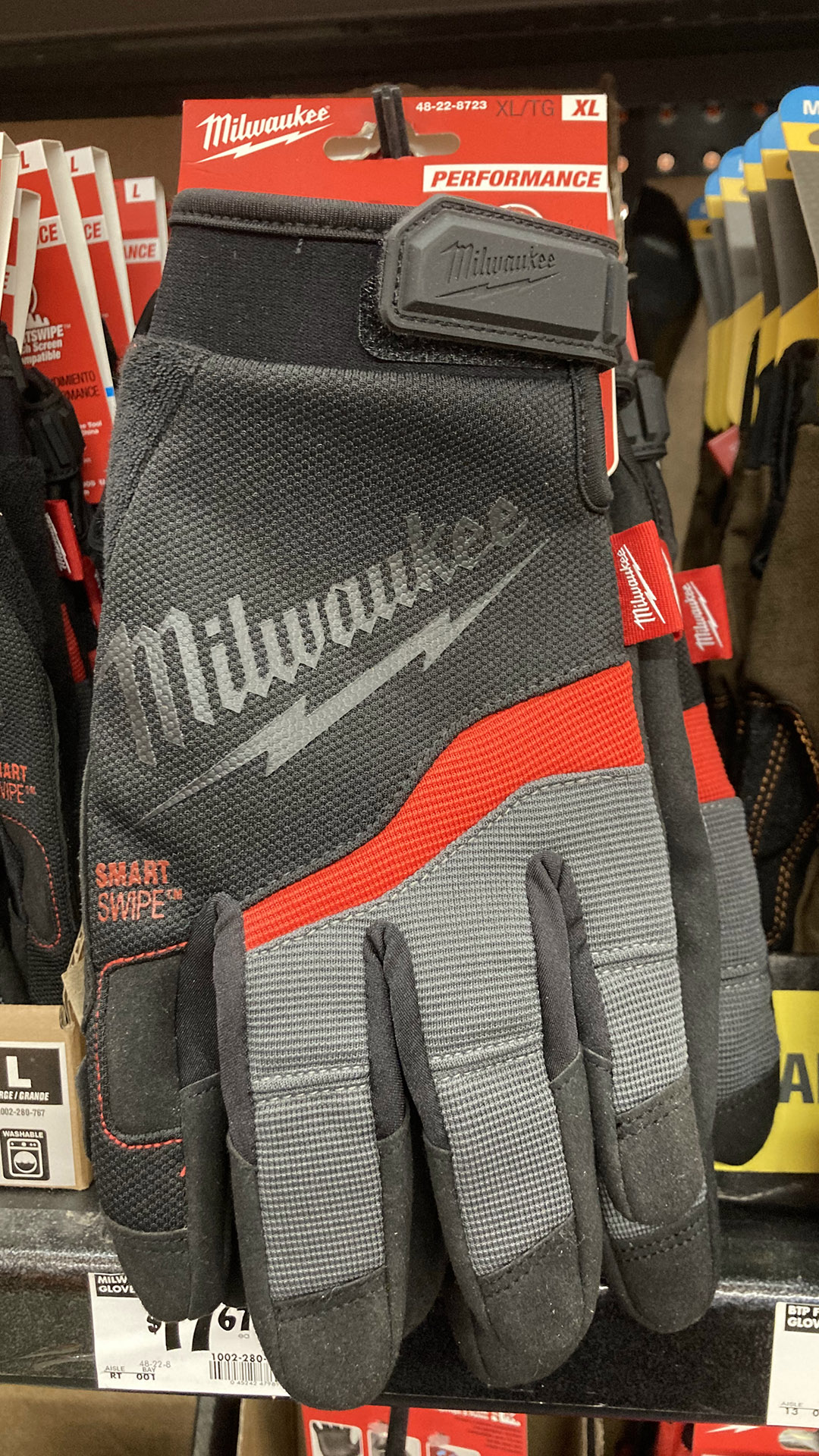 Work gloves in the XL size and with Velcro wrist-fasteners are arranged on hangers on a shelf, with its price on a sticker below.