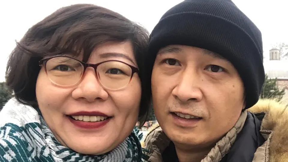 Shi Minglei and Cheng Yuan pose for a selfie portrait while standing outside, with a building and trees in the background.