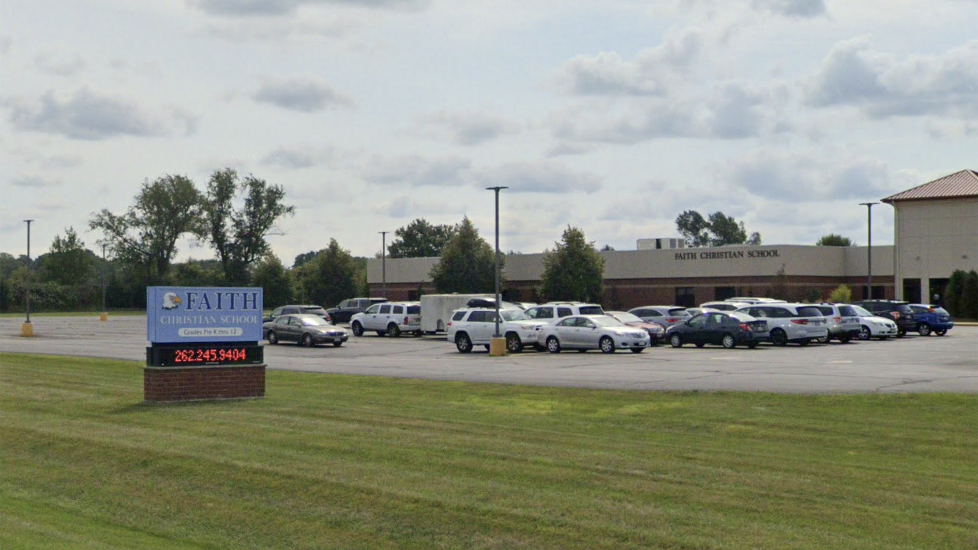 A Google Maps photo shows more than a dozen vehicles parked in a lot in front of a building with a sign reading "Faith Christian School," with a mown lawn in the foreground and another sign with the name "Faith Christian School" alongside an illustration of a bald eagle's head and a digital display showing a phone number.