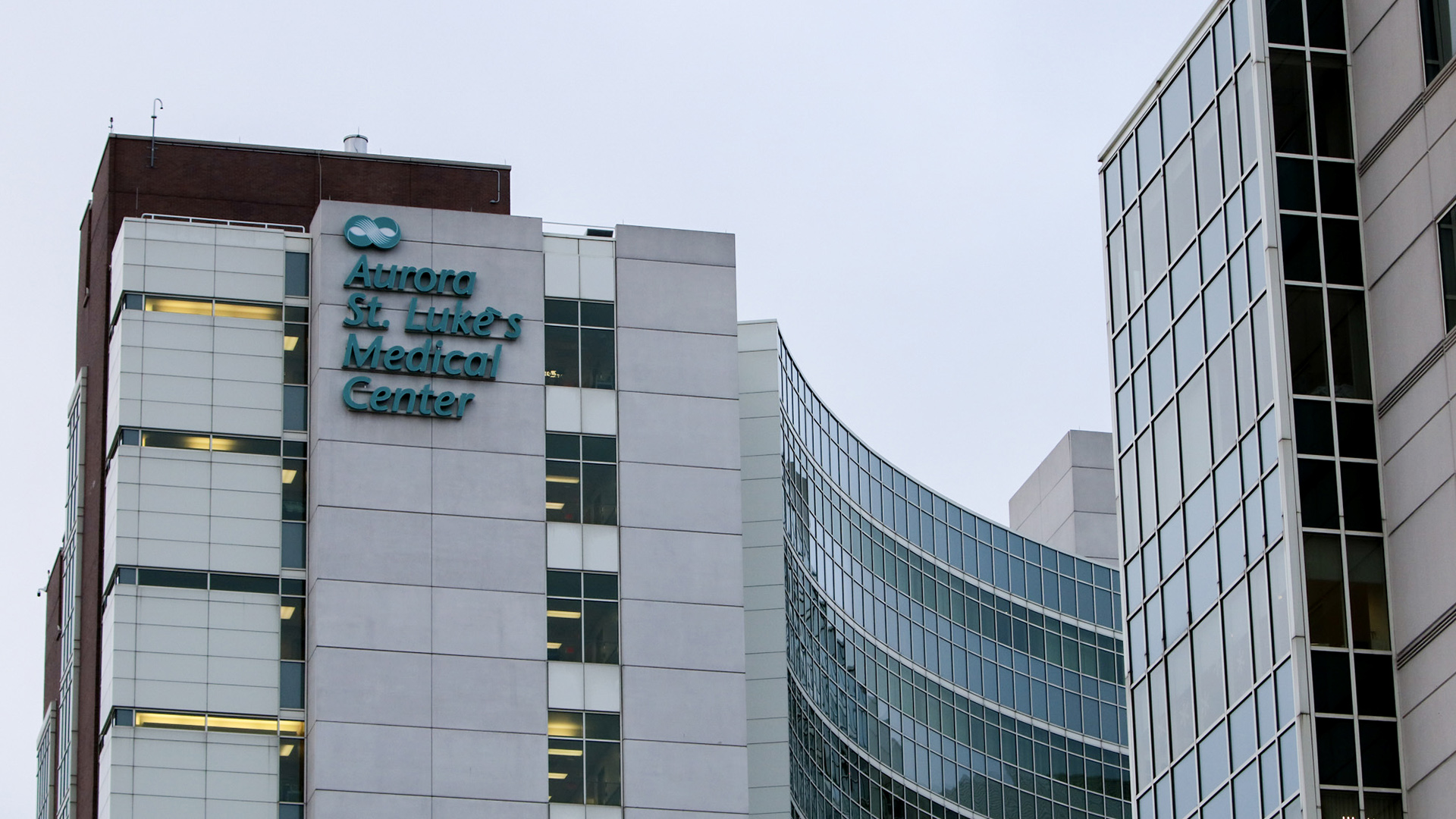 A multi-story building with large glass windows includes a letter sign near its roof that reads "Aurora St. Luke's Medical Center."