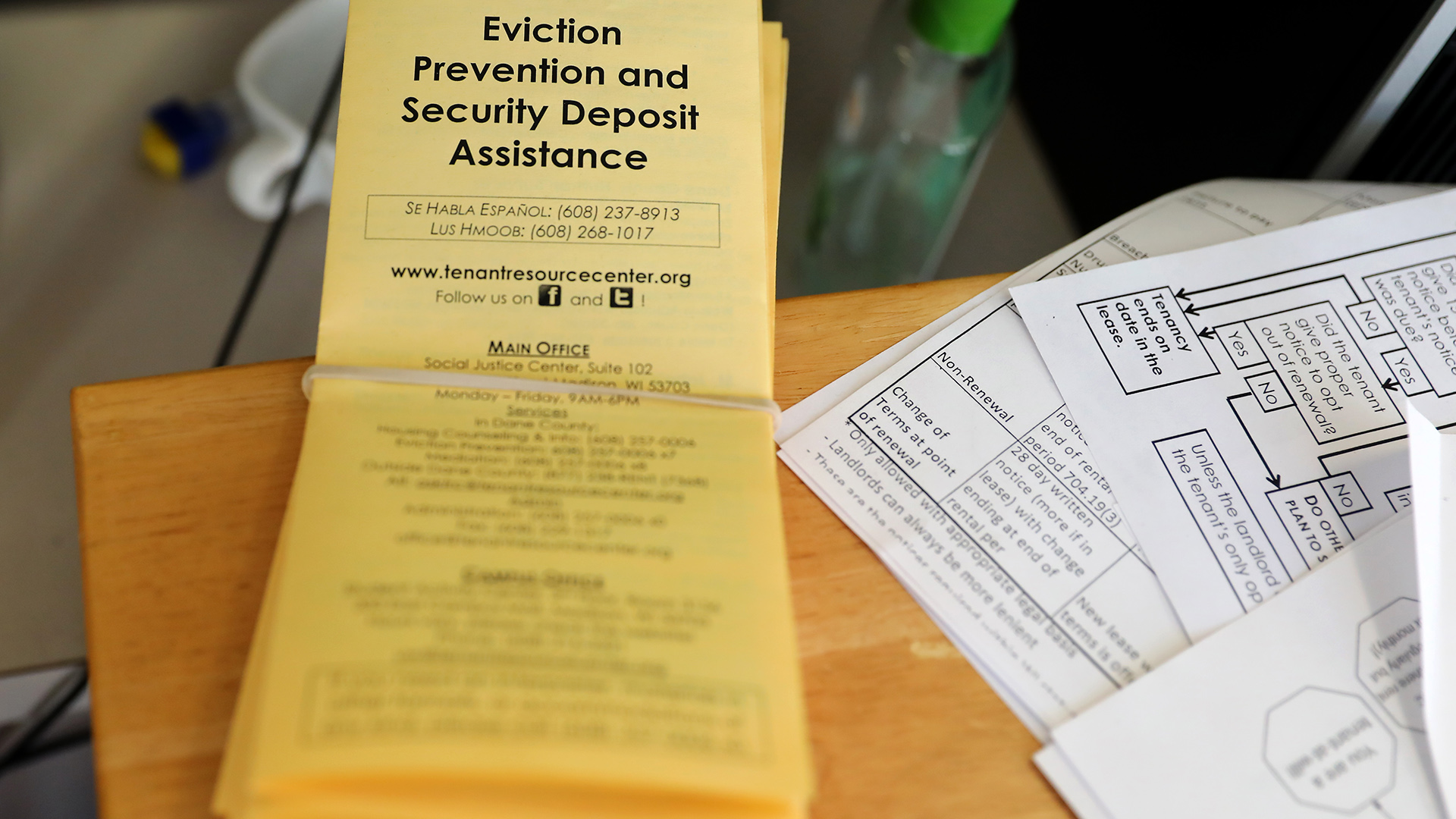 A stack of pamphlets with the title "Eviction Prevention and Security Deposit Assistance" sit on the top of a table next to other papers showing tables and flowcharts related to the eviction process.