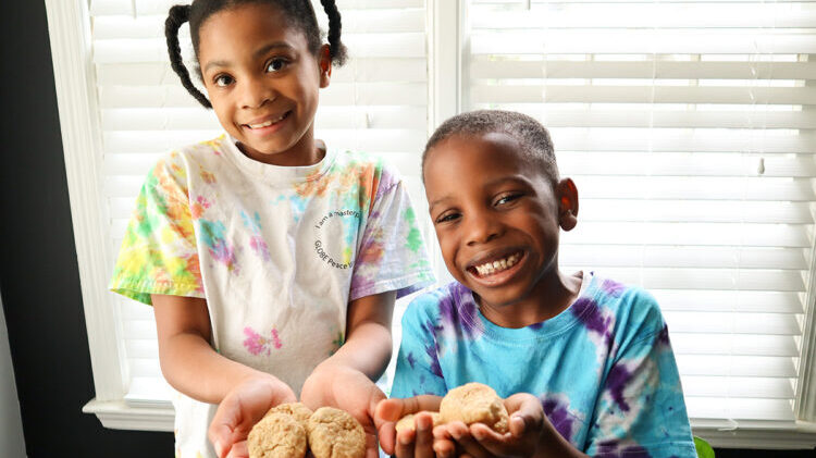 Two children are holding homemade cookies and smiling at the camera.