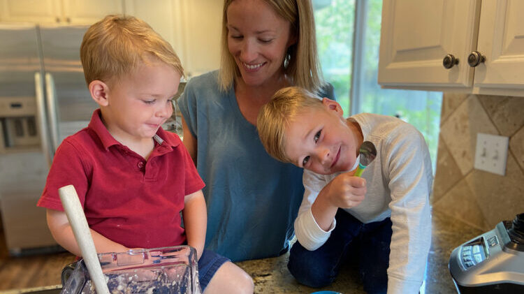 A parent and two children are in a kitchen with a blender and homemade ice cream.