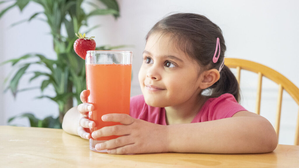 A child sits at a table with a glass of pink lemonade.