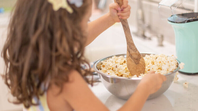 A child is stirring popcorn and other ingredients in a bowl.