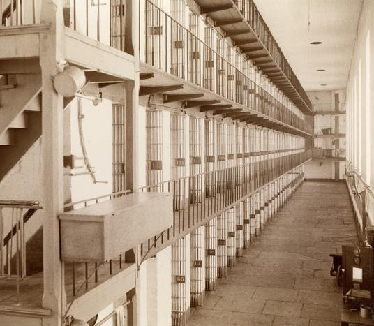 A black and white photo of a hallway of prison cells.