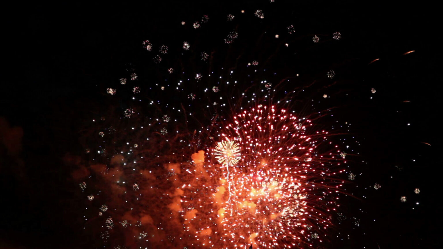 Multiple aerial fireworks explode during a display in a dark night sky.