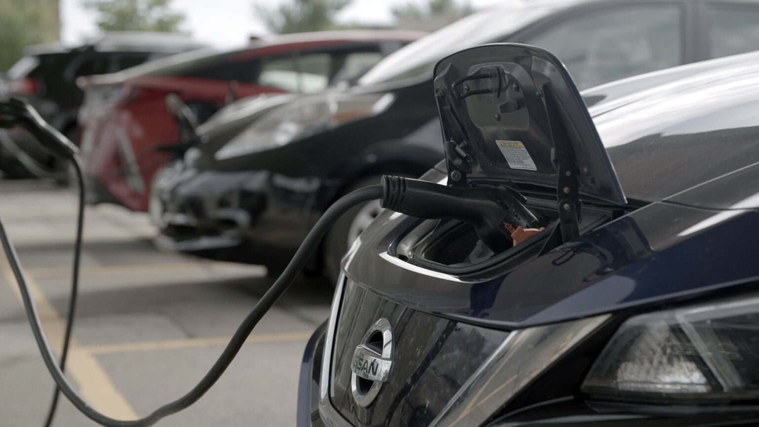 A charging system is plugged into the front of an electric vehicle, with more electric vehicles charging in the background.