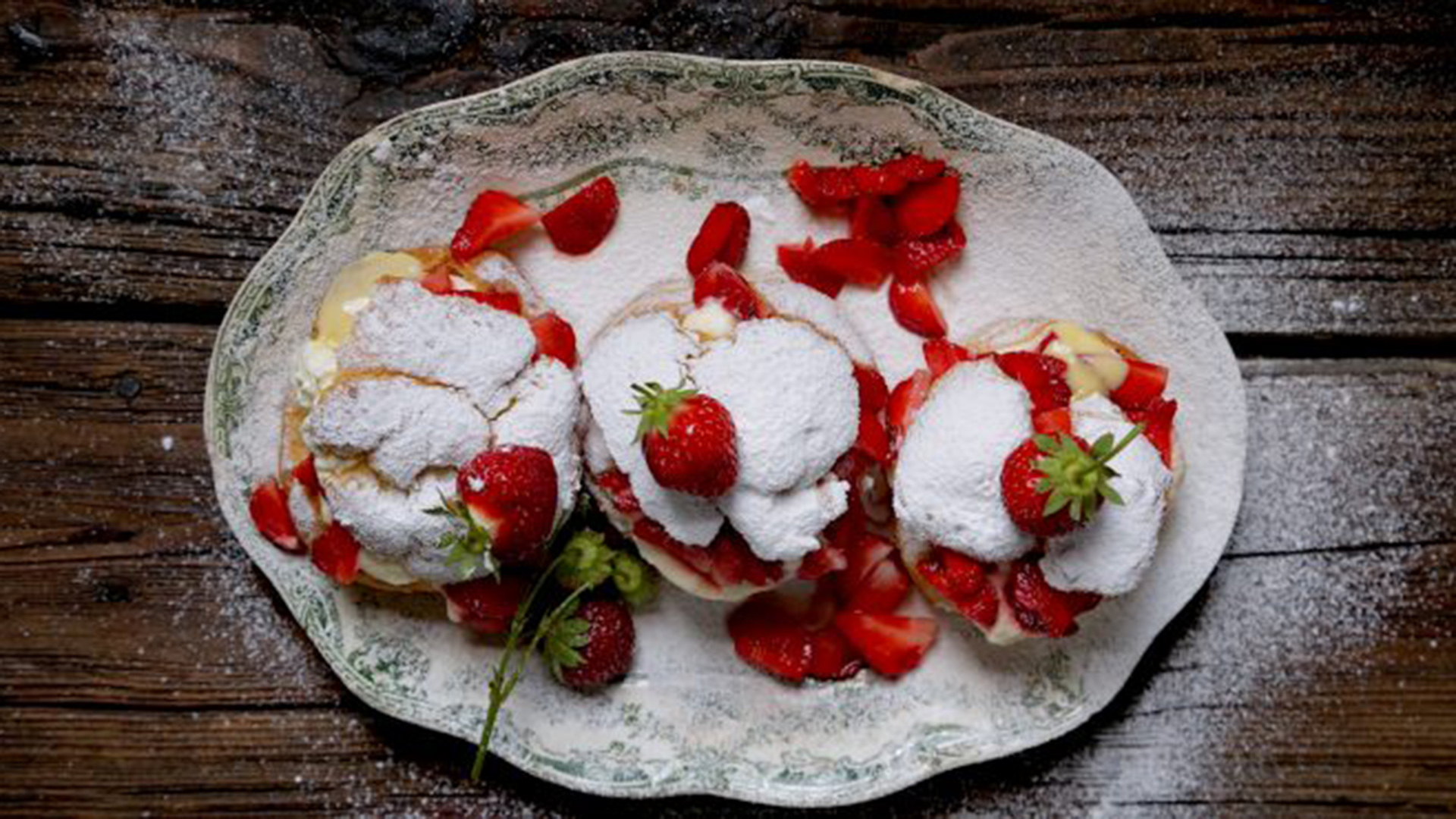 A tray of creampuffs covered in whipped cream and strawberries.