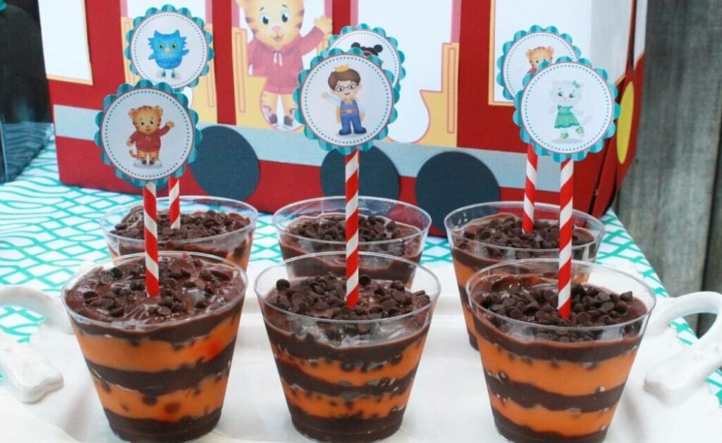 Six brown and orange striped pudding parfaits in clear plastic cups are sitting on a tray. 