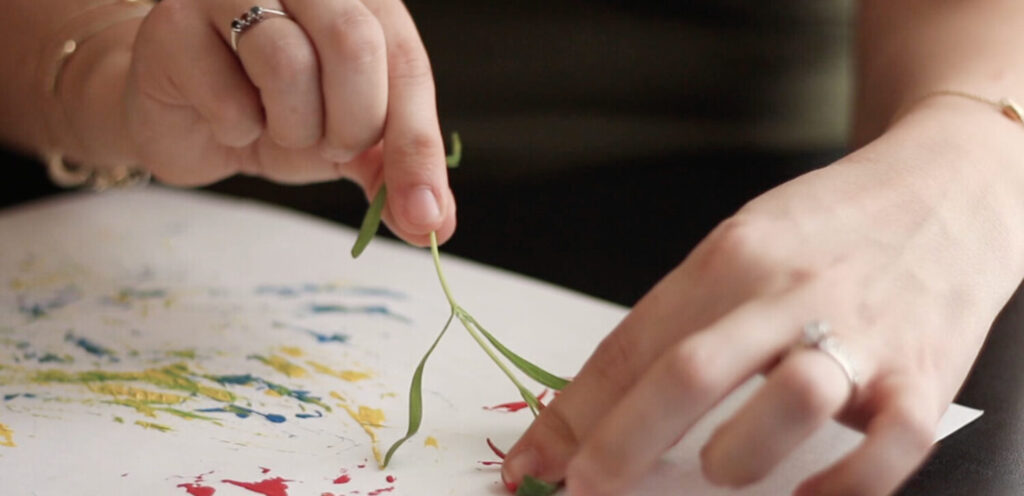 A grown up paints on a piece of paper with a small tree branch