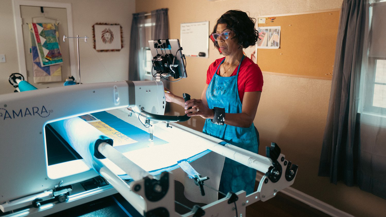 A woman stands at a longarm quilting machine.