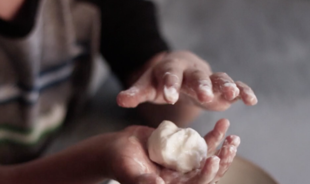 Close-up of a child's hands as they roll dough to make a ball.